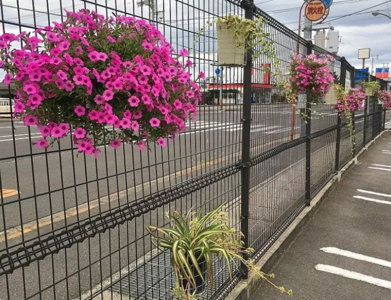 都市部のフェンスに花を飾ることで、無機質な景観に彩りを加え、地域に安心感と温かみをもたらす「花と緑のまちづくり」の実践例を示しています。通行人の目に触れることで、犯罪抑止にもつながる可能性があります。